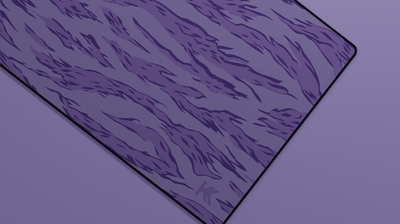 Close-up of the right side of the Purple Tiger Camo Deskmat showing bold stripe pattern, hemmed stitching, and surface texture.